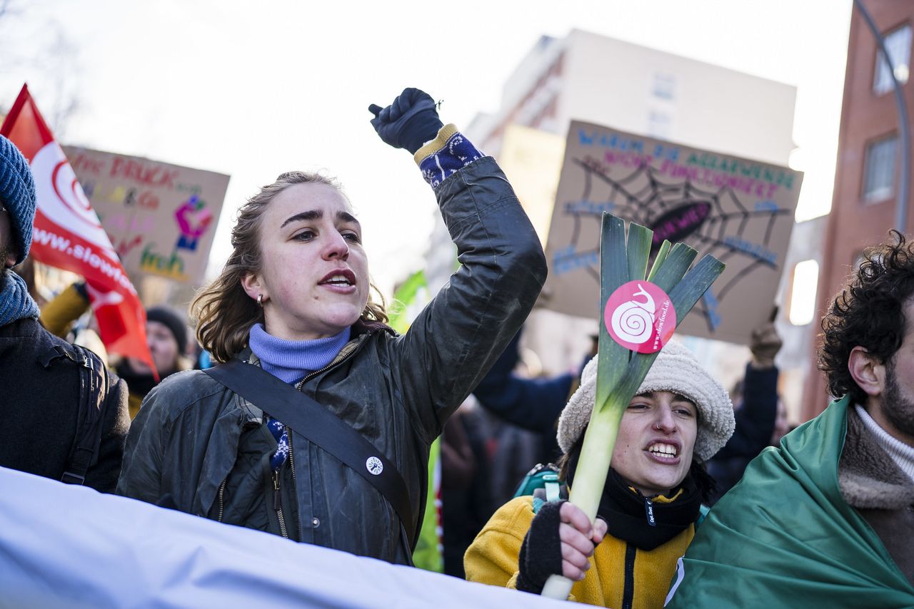Junge Demonstrierende rufen ihre Forderungen. Man sieht im Hintergrund Demoschilder. Zentral stehen zwei Frauen, eine streckt die Faus nach unten, die andere hält eine Lauchstange mit dem Slowfood-Logo.